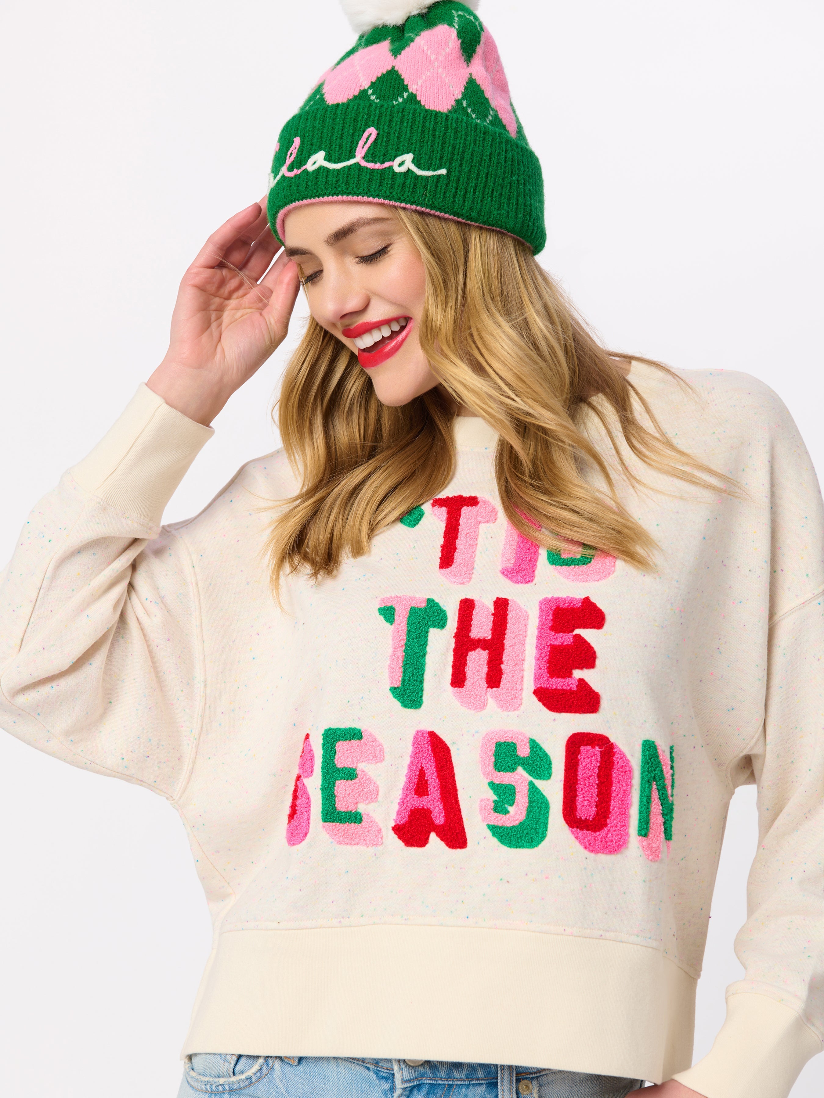 Model wearing cream Tis the Season relaxed sweatshirt with colorful chenille lettering and holiday beanie