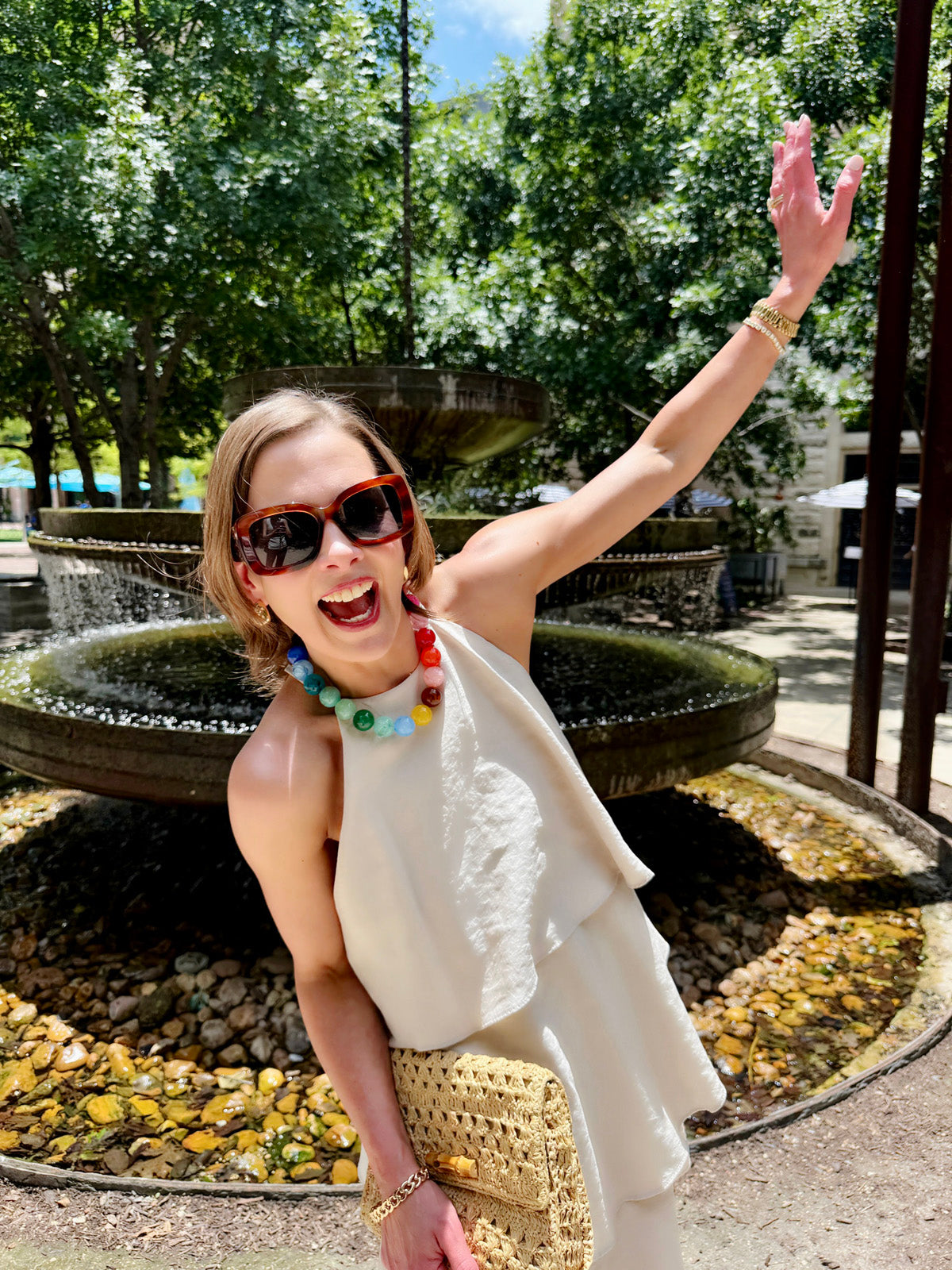 Woman wearing colorful rainbow multi beaded necklace with white top near fountain outdoors