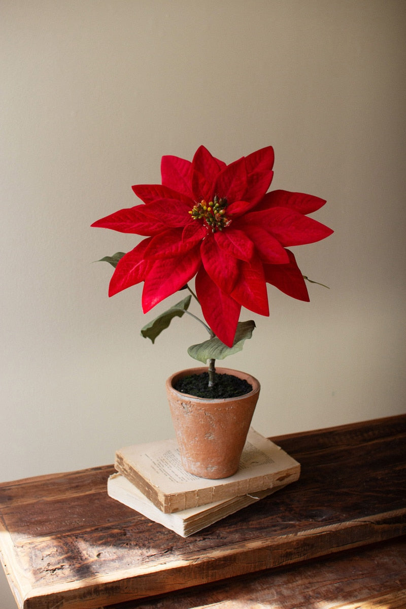 Red poinsettia artificial flower in a rustic terracotta cement pot on stacked books
