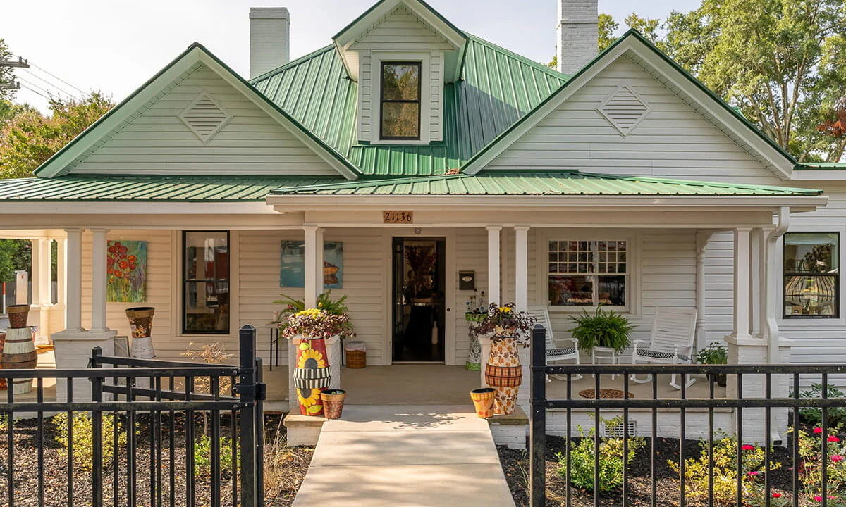 Charming white cottage building with green metal roof and welcoming front porch at Inspired at Lake Norman
