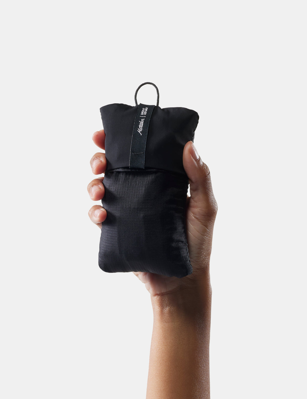 Hand holding a compact black Matador sleep mask and earplugs packed into its pouch