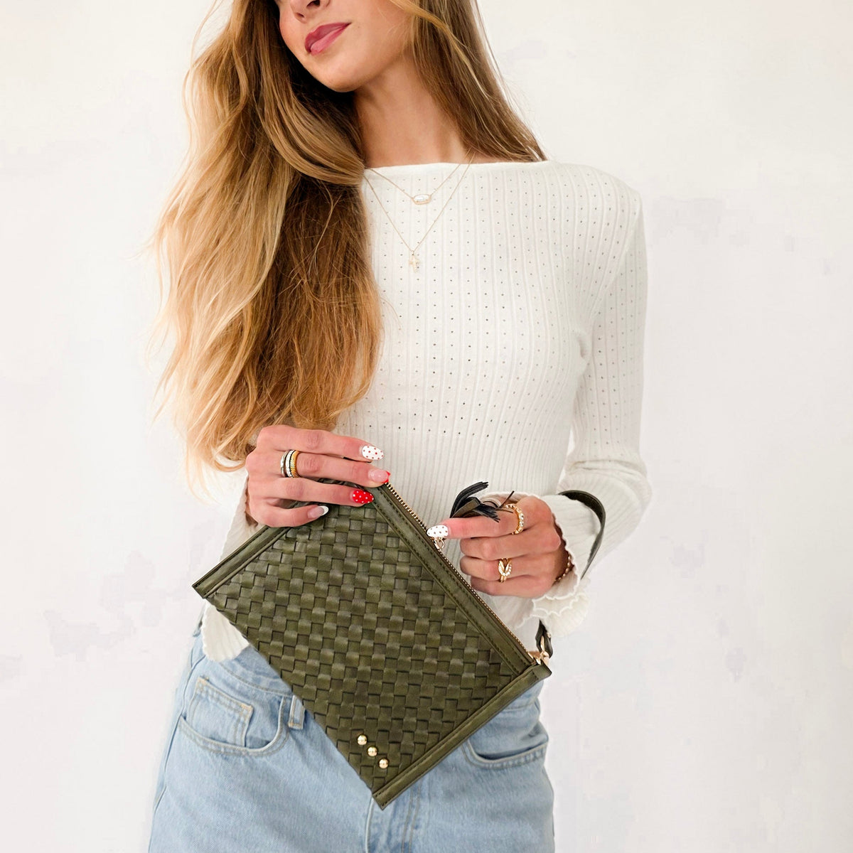 Model holding olive green woven leather clutch crossbody bag while wearing white top and jeans