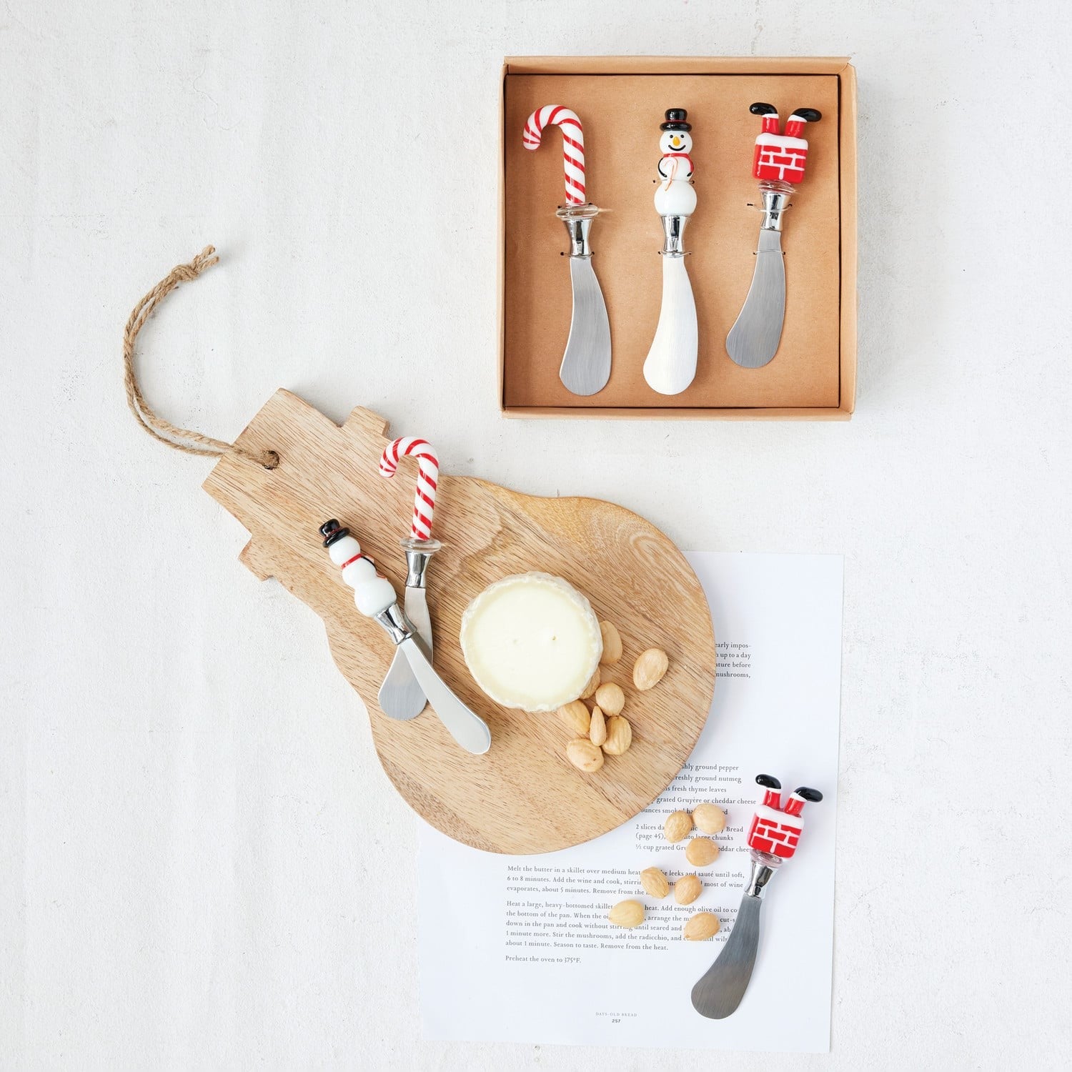Set of three Christmas-themed spreaders with candy cane, snowman, and chimney handles displayed with cheese board