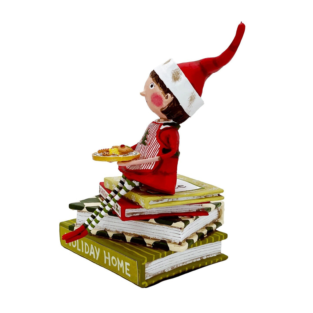 Elf figurine in red outfit sitting atop stacked holiday books holding cookie tray
