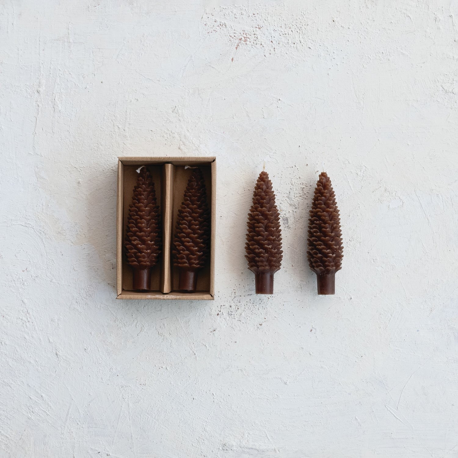 Set of two 5.5 inch brown pinecone-shaped taper candles shown in kraft box and beside it