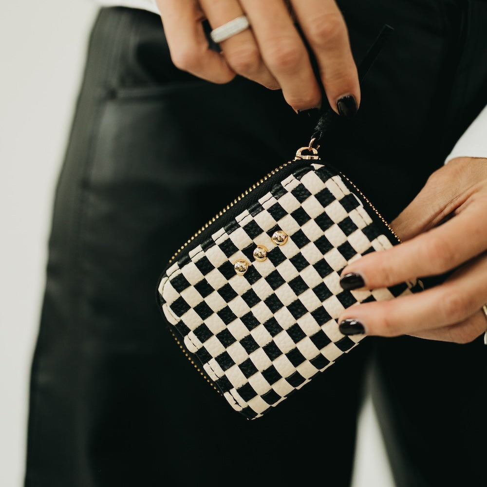 Hand holding a black and white checkered woven zip wallet with gold hardware details