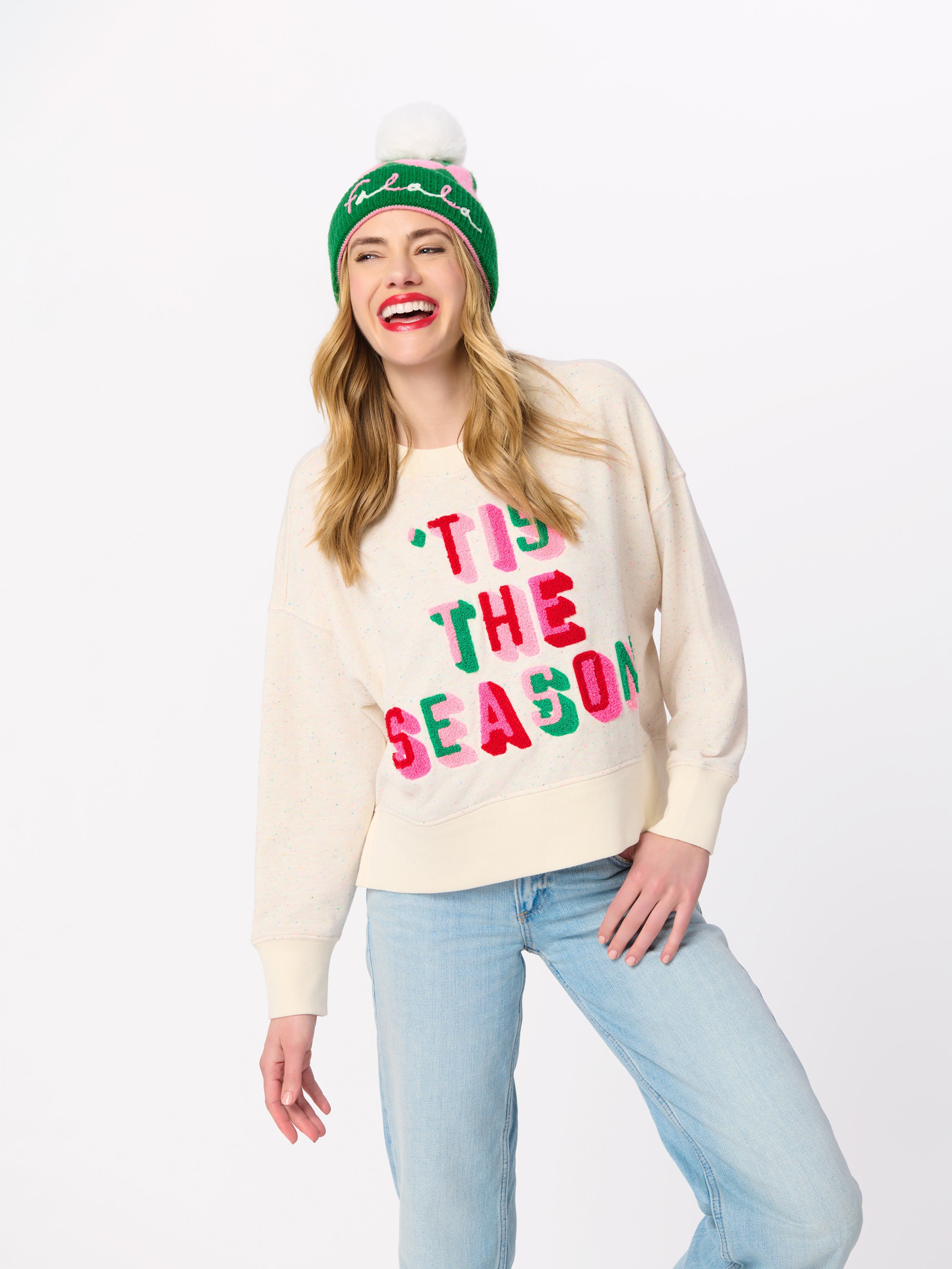 Woman wearing cream Tis the Season sweatshirt with green Falala beanie and jeans