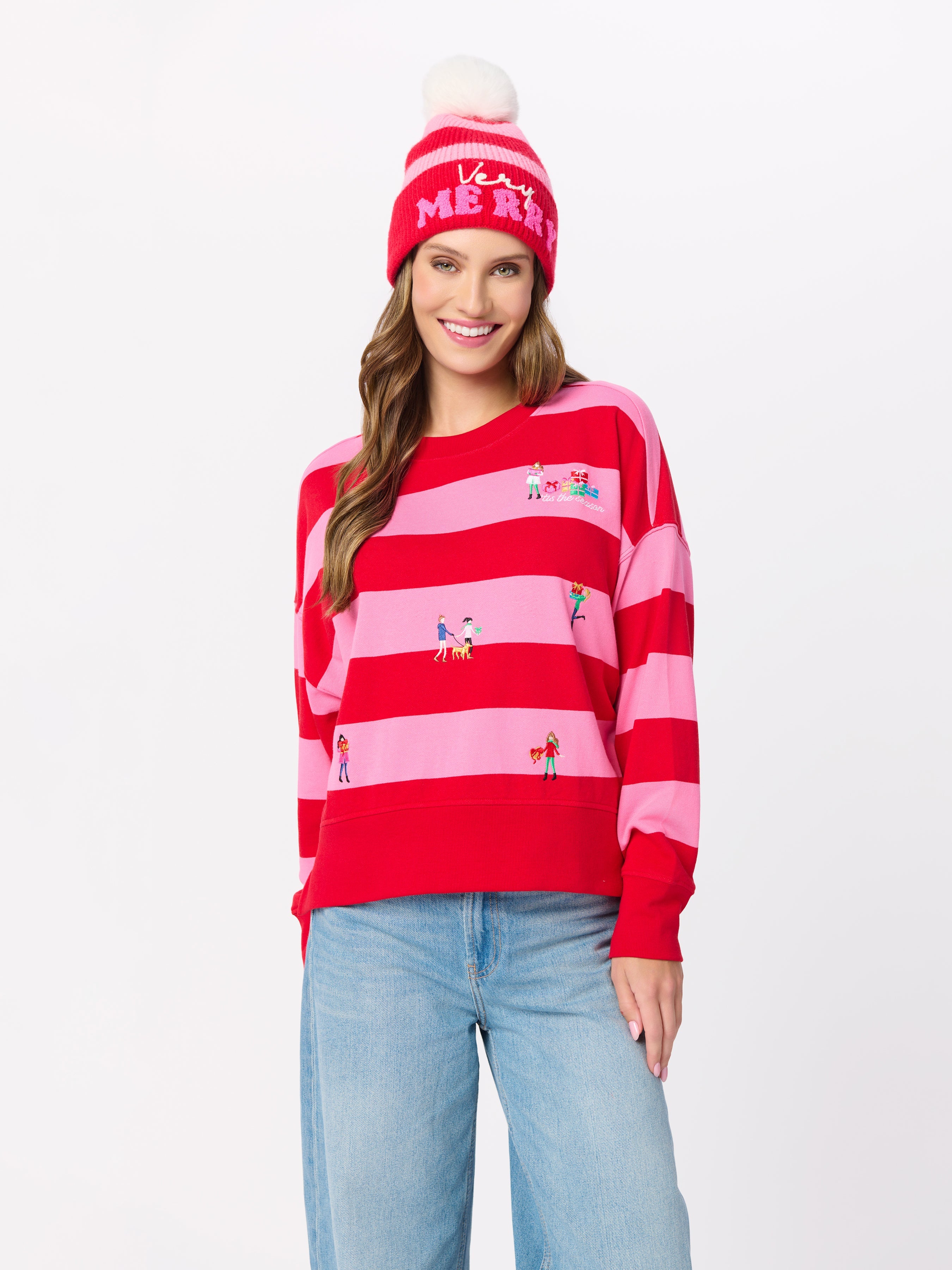 Model wearing red and pink striped sweatshirt with holiday embroidery and matching beanie hat