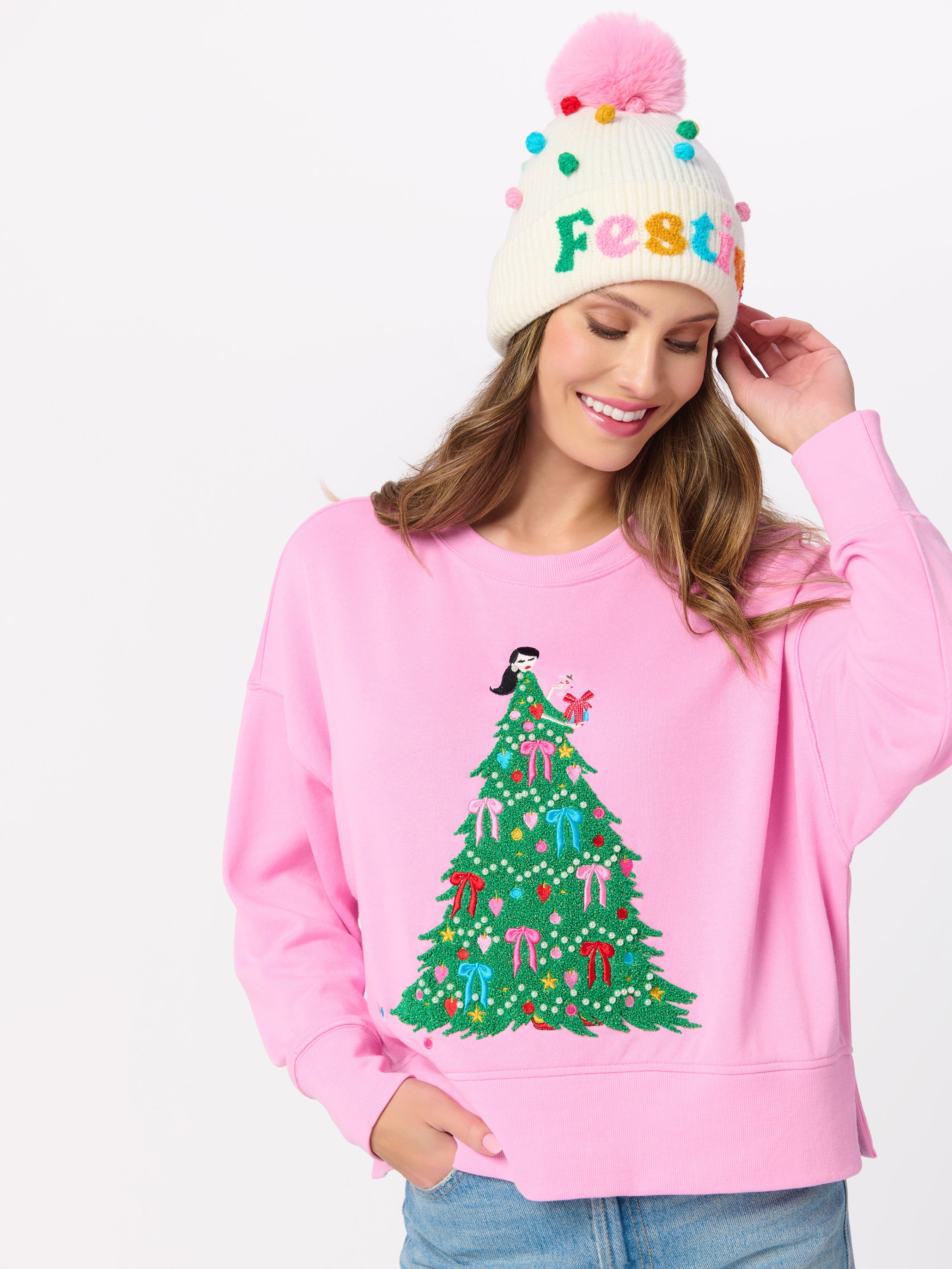 Model wearing pink relaxed sweatshirt with embroidered Christmas tree lady design and festive beanie