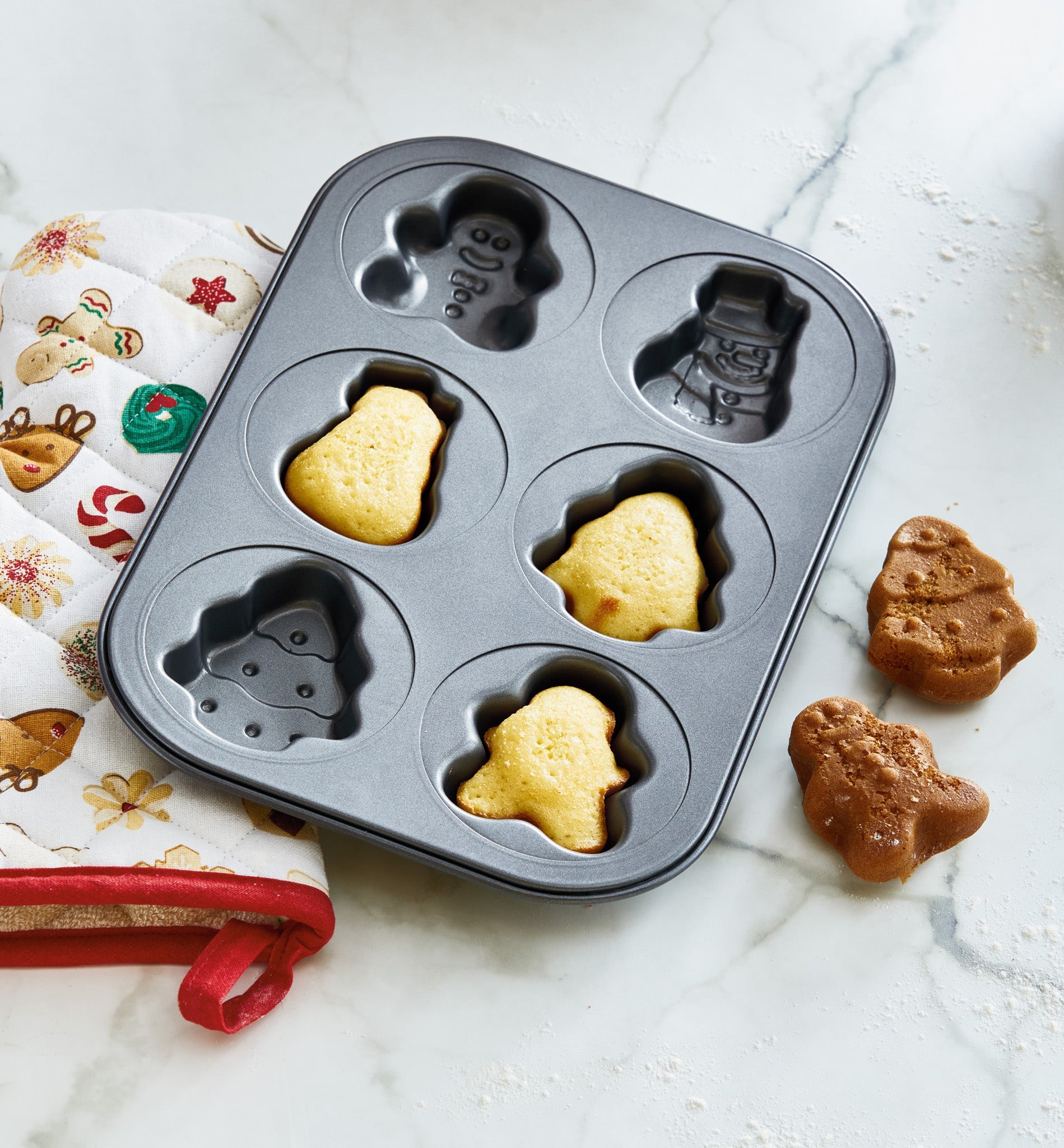 TAG mini Christmas non-stick baking pan with holiday shaped cavities and baked treats on marble surface