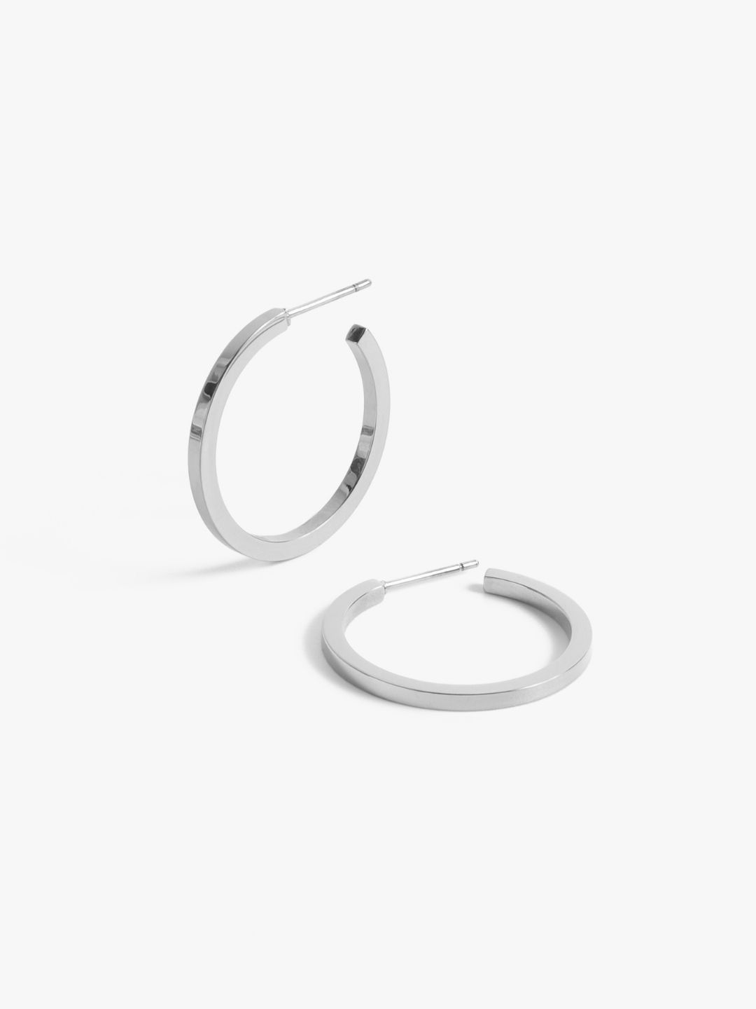 Pair of silver chunky hoop earrings with flat profile and post backs on white background