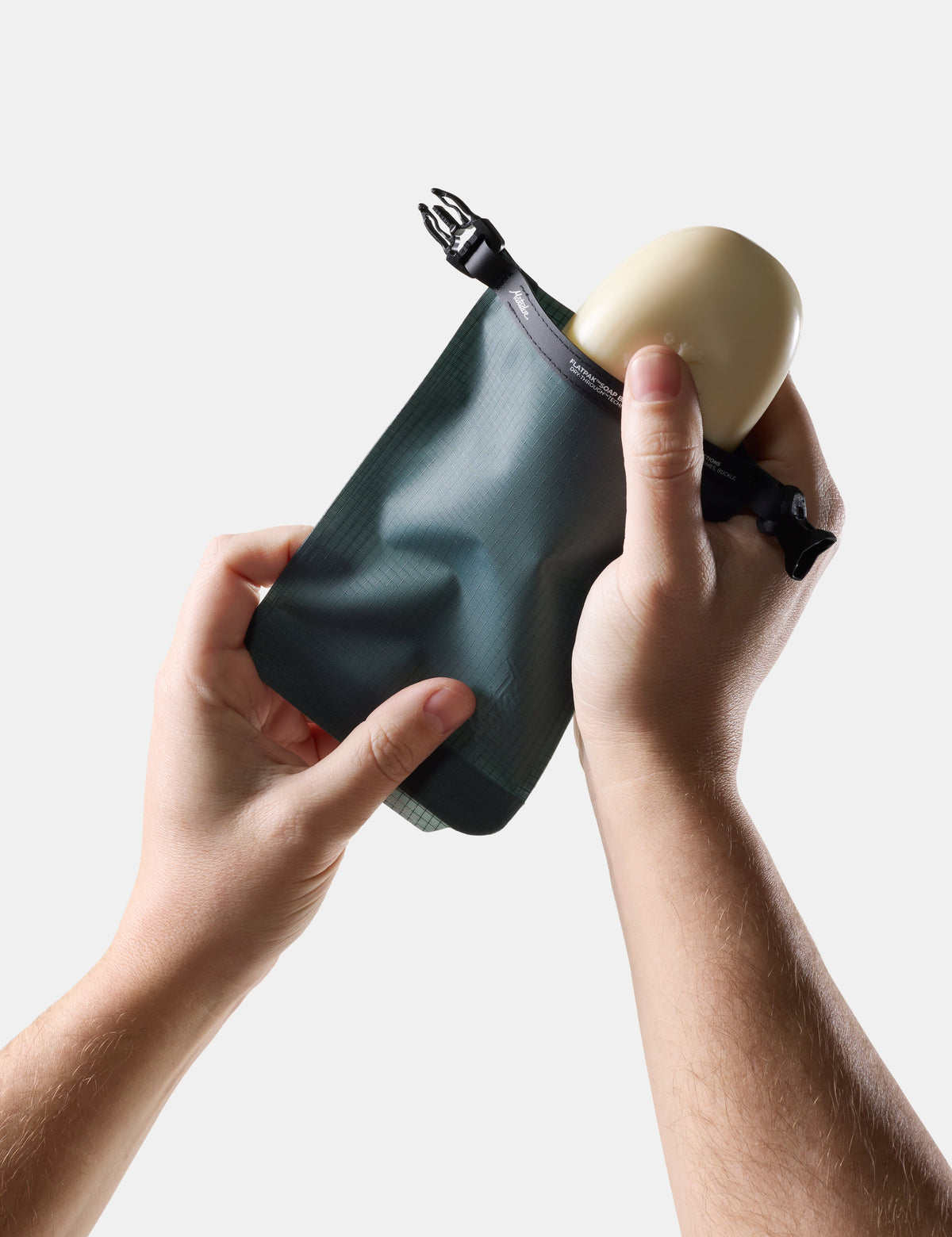Hands demonstrating how to insert a soap bar into the Matador FlatPak Soap Bar Case in Juniper