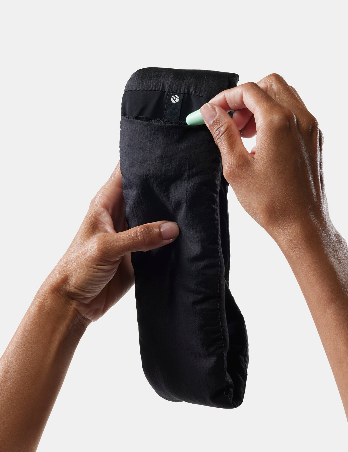 Hands inserting mint green earplugs into pocket of black Matador sleep mask pouch