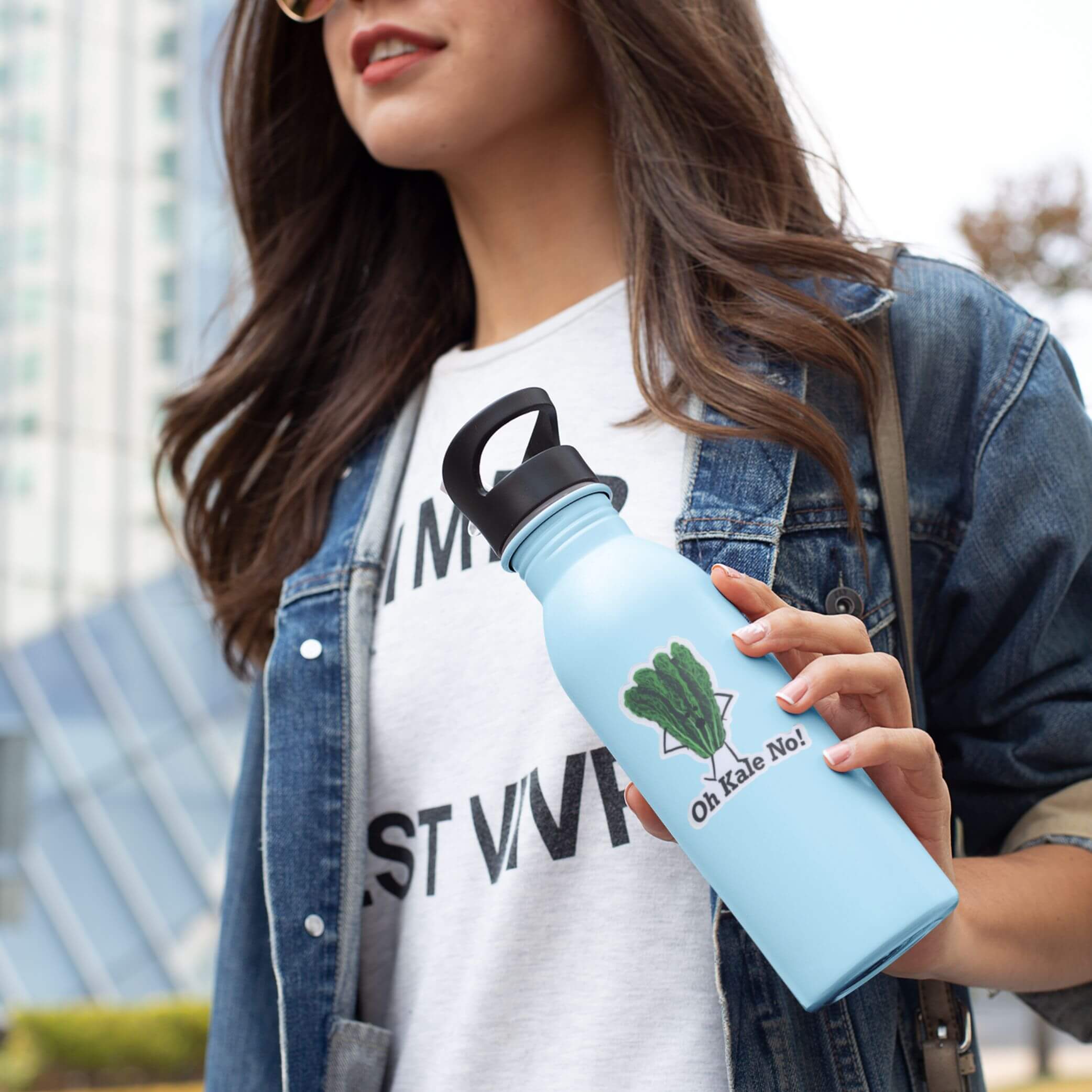 Woman holding a light blue water bottle with Oh Kale No sticker featuring kale illustration