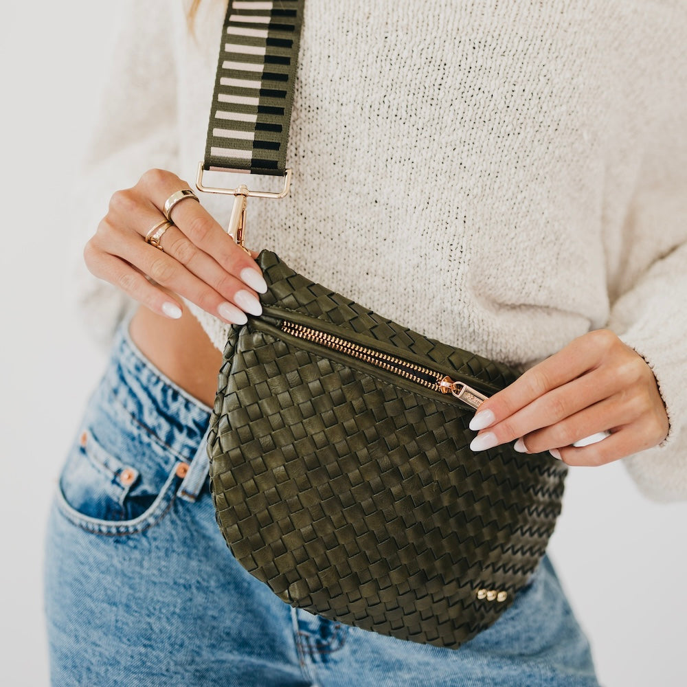 Model holding olive woven leather bum bag with gold zipper and striped crossbody strap