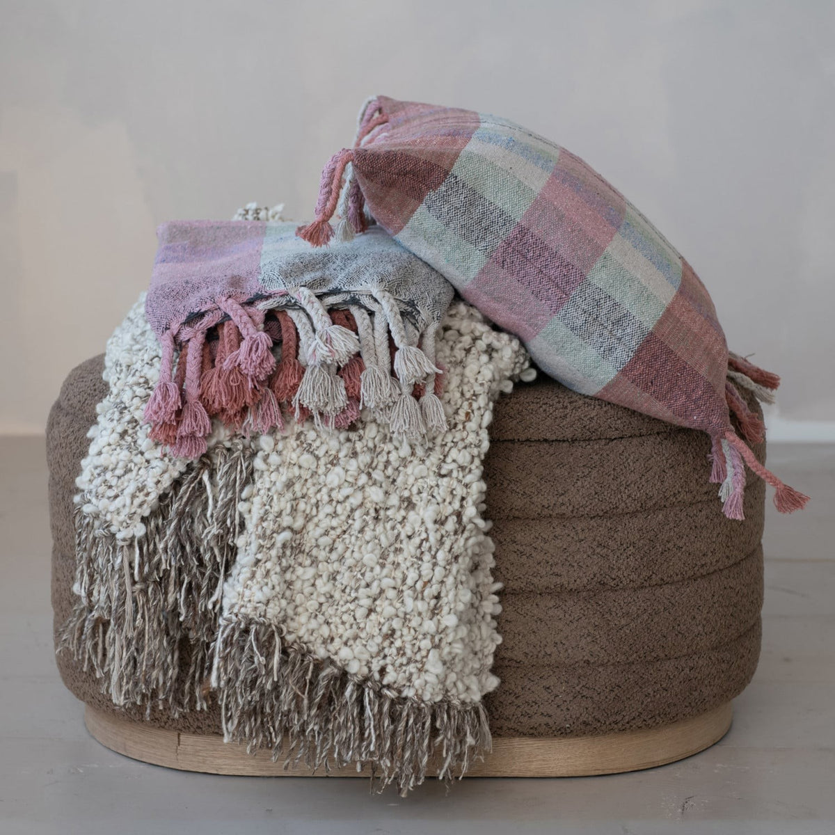 Cream woven wool blend shag throw with fringe draped over a round brown ottoman