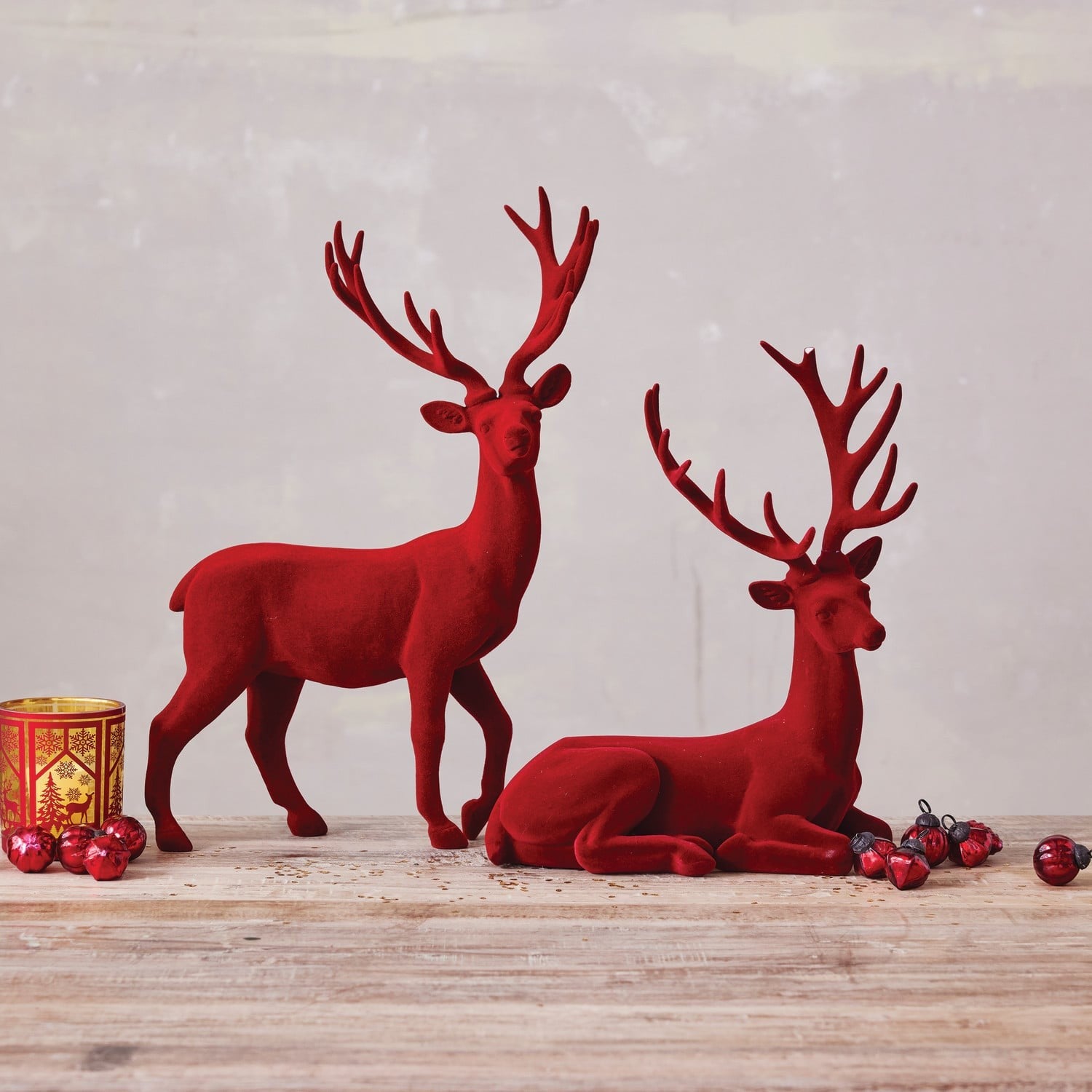 Two burgundy flocked resin deer figurines, one standing and one lying down, with holiday decorations