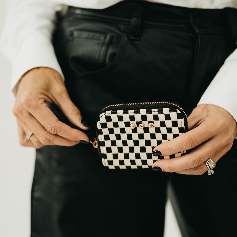 Model holding Pretty Simple Wynona woven wallet in black and white checkered pattern with gold zipper