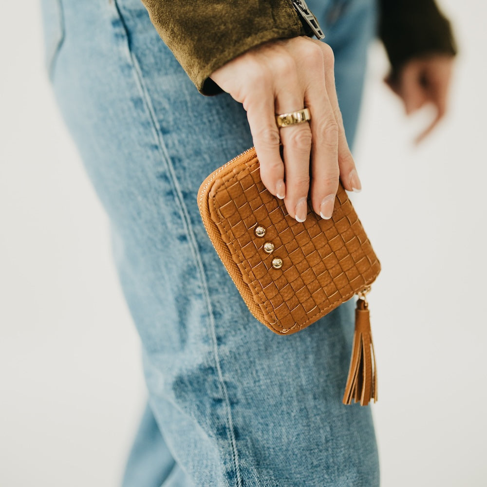 Model holding Pretty Simple Wynona Woven Wallet in brown with gold tassel zipper pull