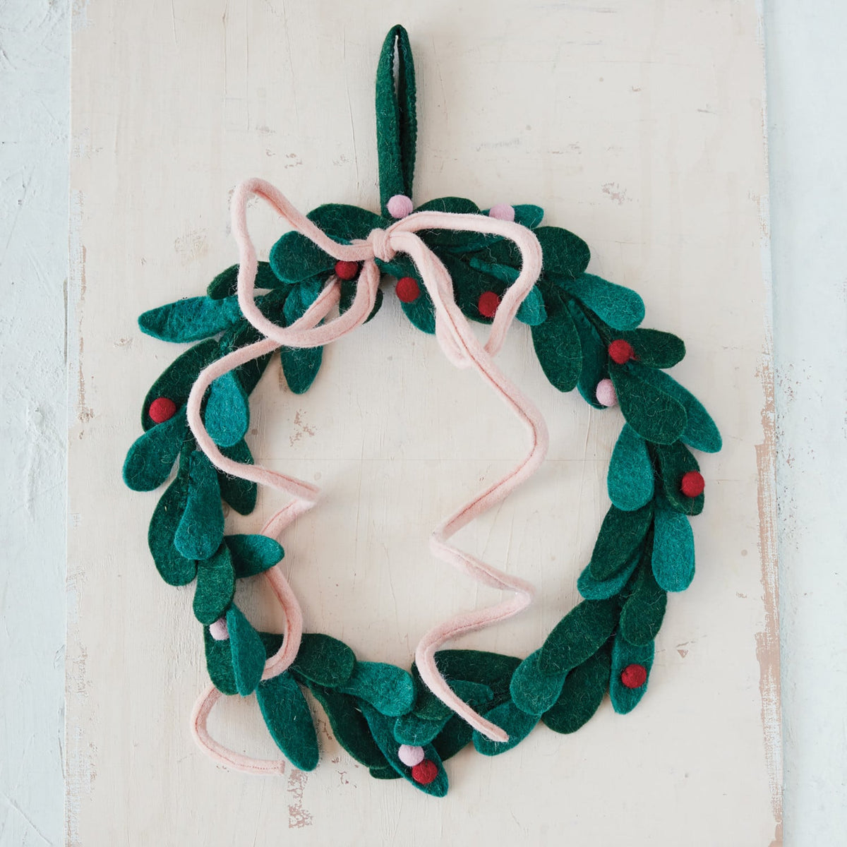 Handmade wool felt green leaf wreath with pink bow and red berries on rustic background